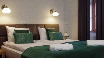 Ein Hotelzimmer mit einem großen Bett, einer grünen Bettdecke, zwei Wandlampen und einem Fenster mit Vorhängen.