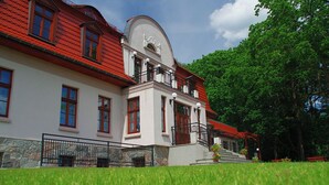 A two-story building with a red-tiled roof, white walls, and a balcony with black railings. - Dwór Uradz (gmina Barwice)