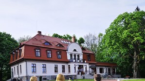 A large, historic building with a red roof and white walls, featuring a central courtyard with outdoor seating. - Dwór Uradz (gmina Barwice)