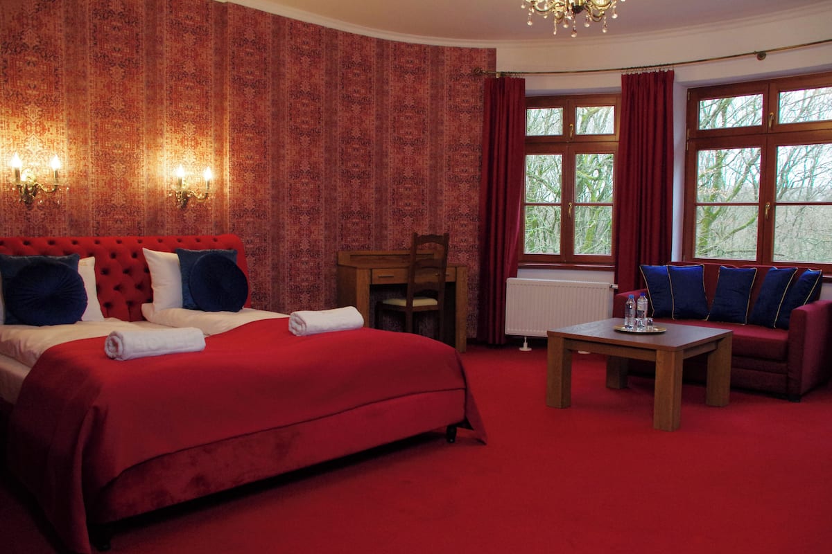 Habitación de hotel con una cama grande, un sofá, una mesa y una ventana con cortinas.
