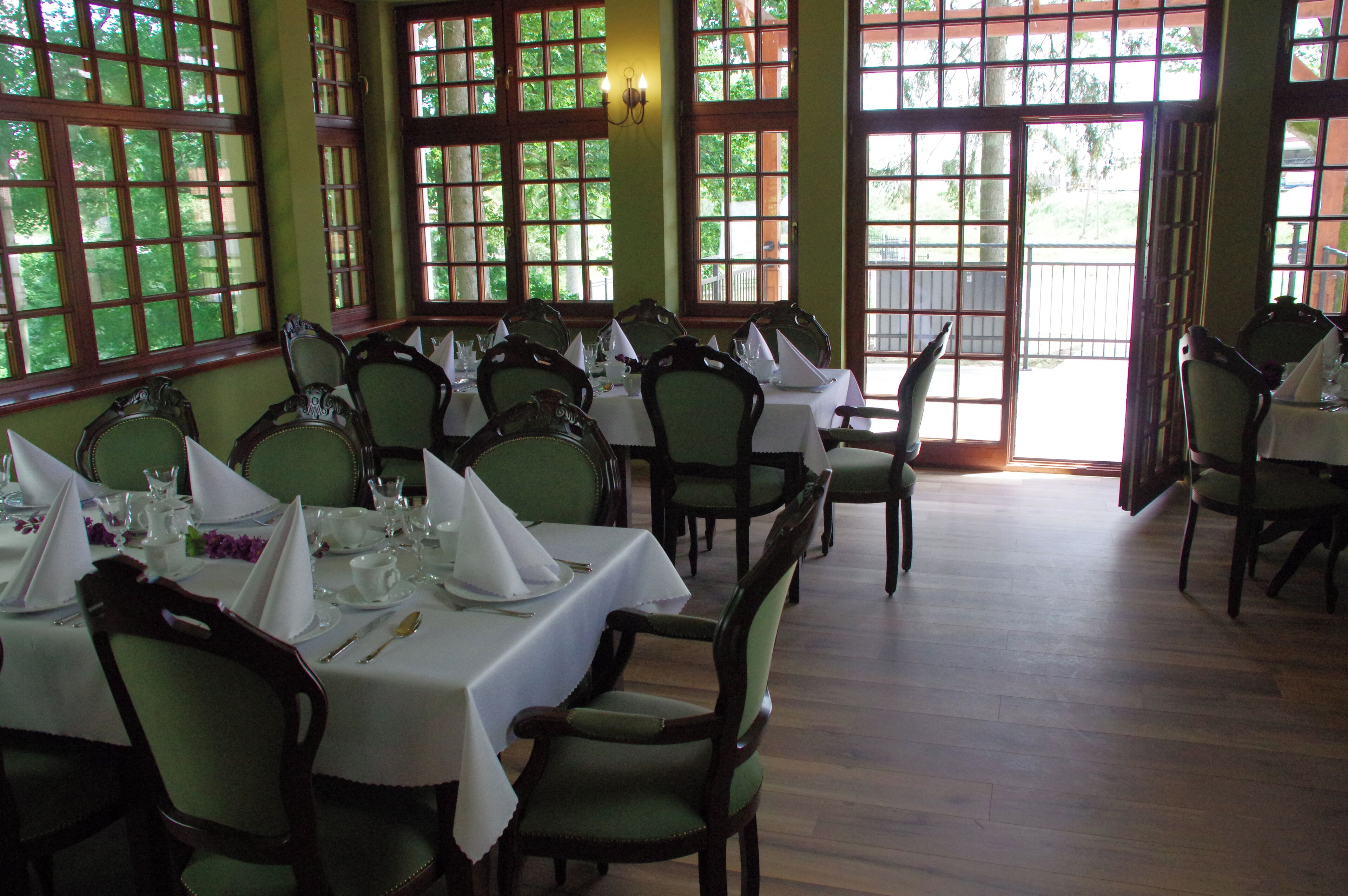 Comedor con mesas dispuestas para una comida, sillas y ventanas amplias con vista a follaje.