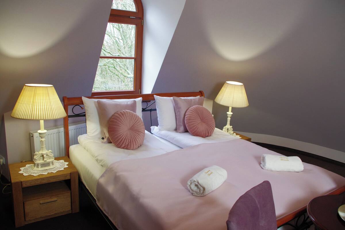 Un dormitorio con una cama, dos lámparas de noche, una ventana y una mesita de noche.