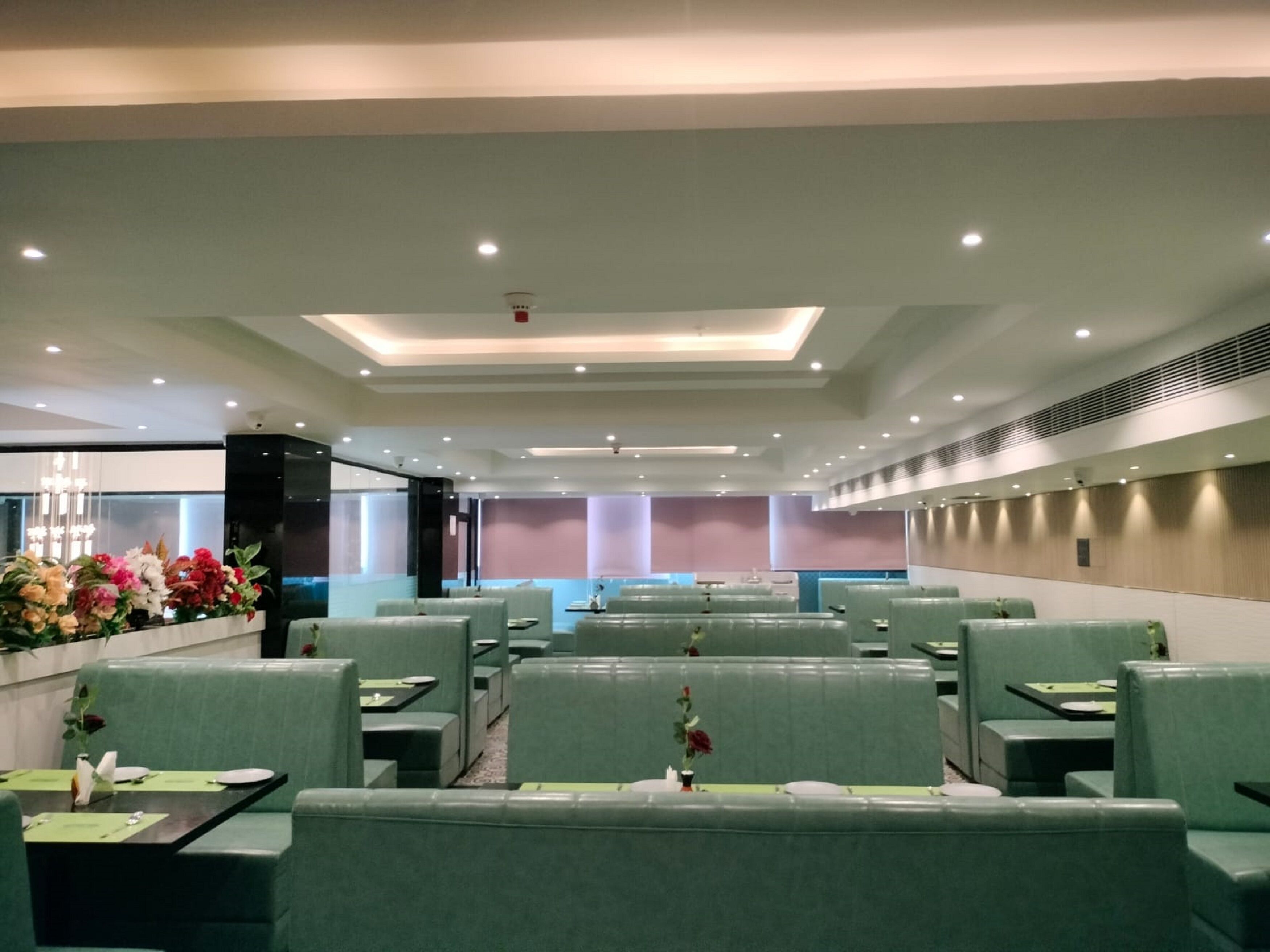A modern restaurant with green upholstered booths, recessed ceiling lighting, and a floral arrangement on the left.