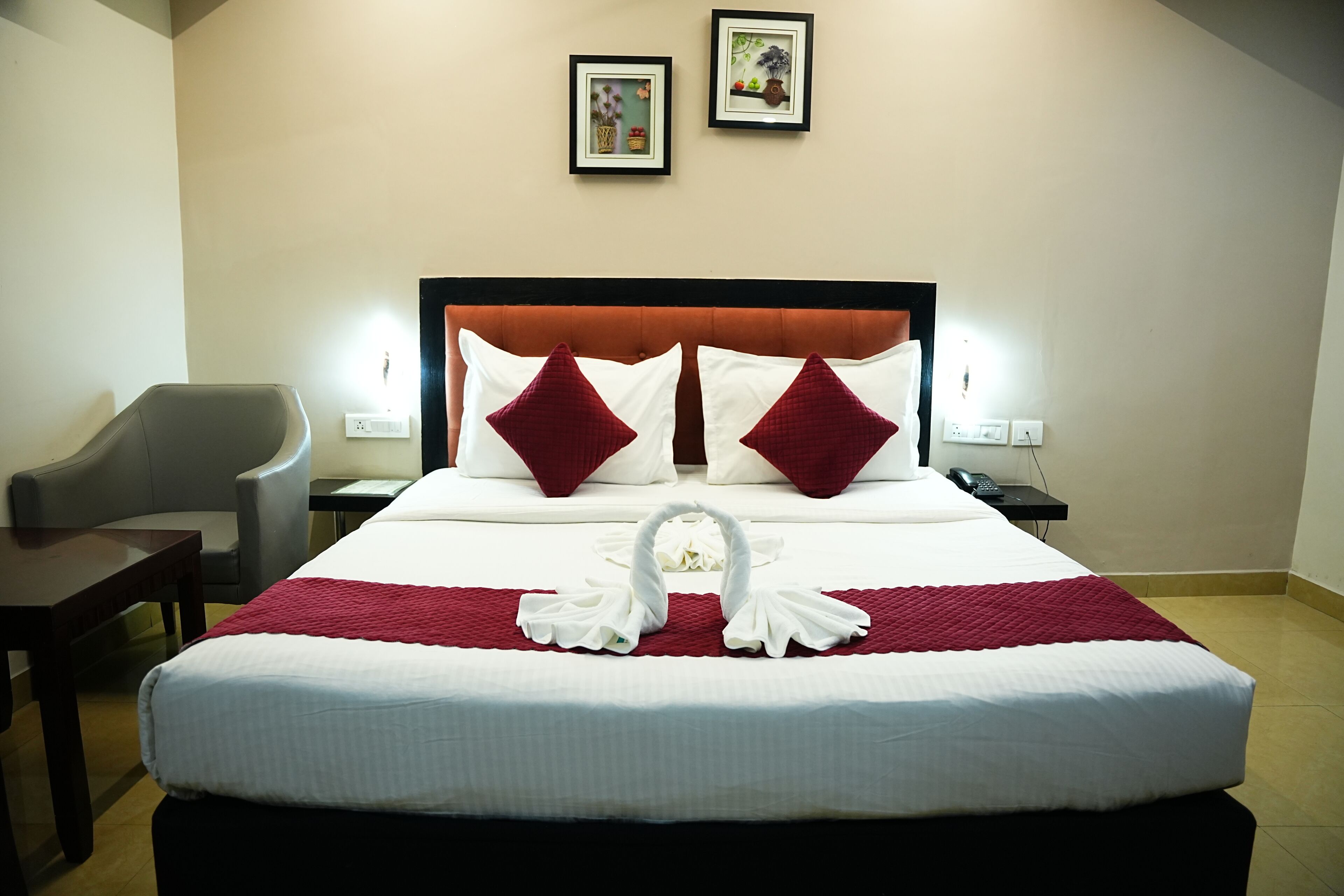 Quarto de hotel com uma cama bem arrumada, uma cadeira, uma mesa de cabeceira e duas molduras na parede.