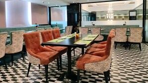 Un espace repas moderne avec un sol à carreaux, une longue table recouverte de sets de table verts et des chaises à l’assise orange.