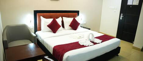 A hotel room with a bed, a desk, a chair, and a door.