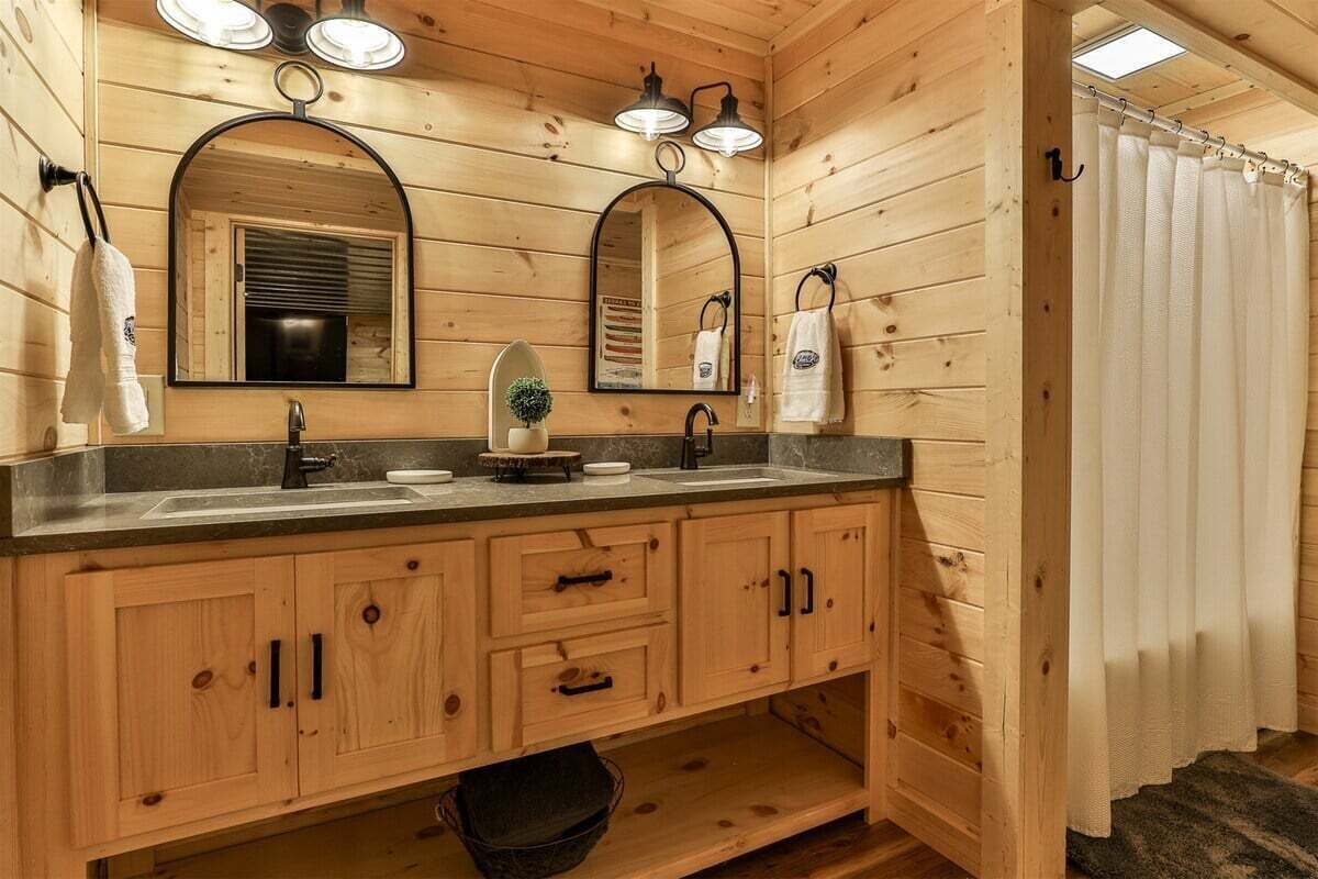Une salle de bain de style rustique, avec des murs en bois, un meuble-lavabo à deux vasques, des armoires en bois et un miroir.