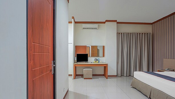 A hotel room with a wooden desk, a bed, a small stool, a mirror, and a window with curtains. - Collection O 90724 Hotel Sinar Sidoarjo (Sidoarjo)
