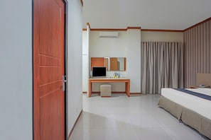 Une chambre d’hôtel avec un bureau en bois, un lit, un petit tabouret, un miroir et une fenêtre avec des rideaux.