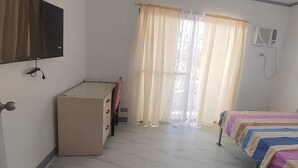 Un dormitorio con cama, escritorio, silla, televisor y ventana con cortinas.
