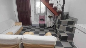 Una habitación con piso a cuadros, un sofá, una silla, una mesita con un florero y una escalera.