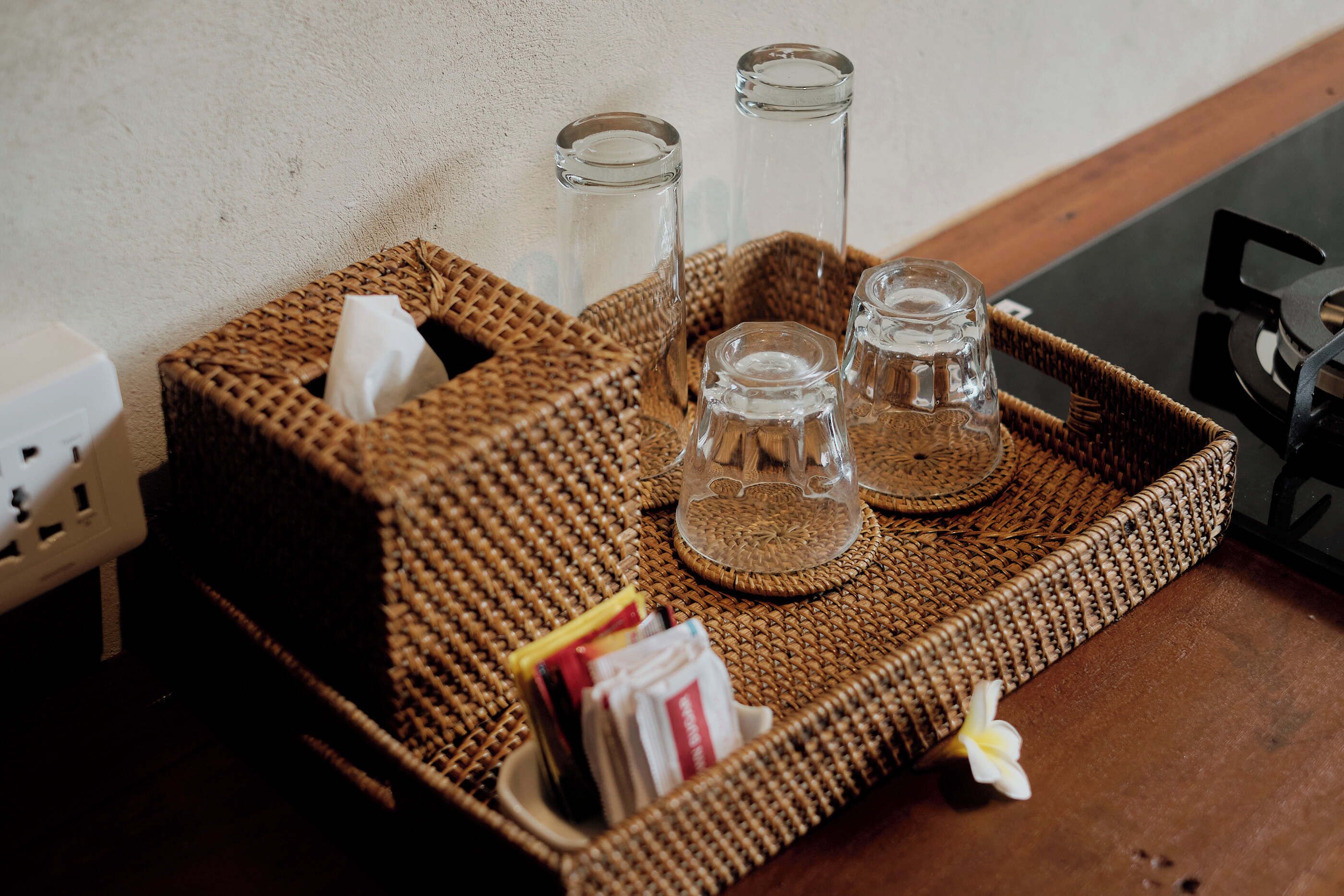 A woven tray with two glasses and a tissue holder on a wooden table.
