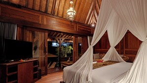 A wooden room with a bed covered in white canopy, a television on a wooden cabinet, and a view of greenery outside. - Tegal Beji Ubud Villa (Ubud)