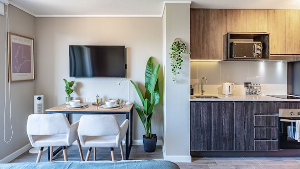 A modern hotel room with a dining area, a TV, a large plant, and a kitchenette. - M&C Departamento Irarrazaval 614 (Santiago)