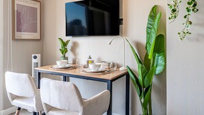 A dining area with a table set for two, a television mounted on the wall, and a large plant to the right. - M&C Departamento Irarrazaval 614 (Santiago)