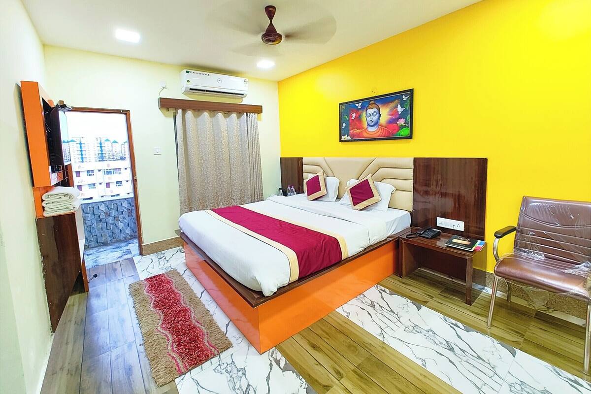 Habitación de hotel con cama, silla, mesita de noche, equipo de aire acondicionado, ventilador de techo y ventana con cortinas.
