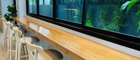 A modern bar area with a long counter and multiple stools, large windows with a view of greenery outside.