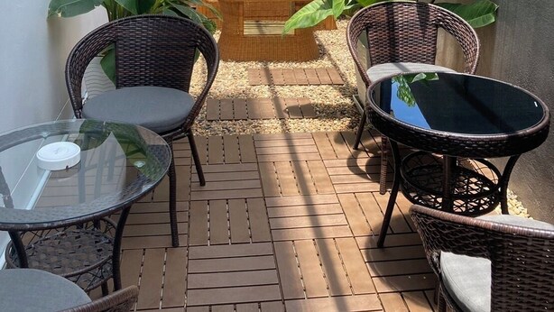 Uma área de pátio aconchegante com móveis de vime, um sofá de madeira e plantas em vasos.
