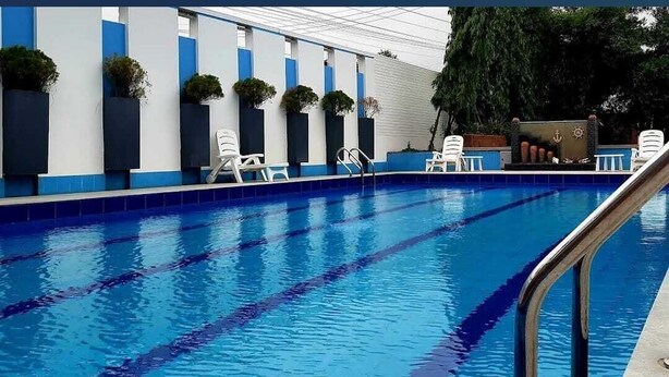 A swimming pool with clear blue water and lane dividers, surrounded by white and blue walls with potted plants and white lounge chairs. - Crow Euro Inn Hotel and Resort (Dhamrai)