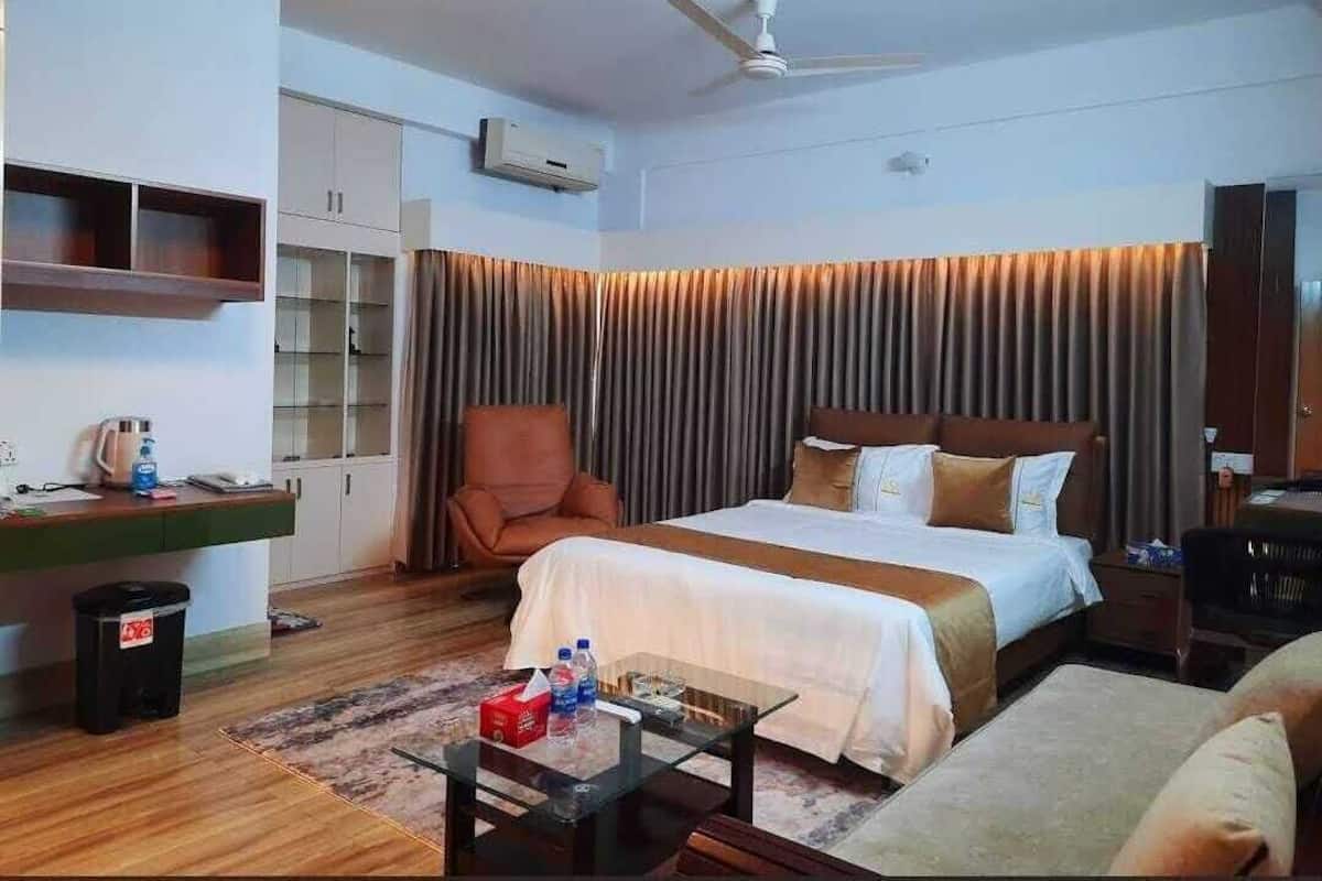 A hotel room with a bed, a desk, a chair, a coffee table, and a ceiling fan.