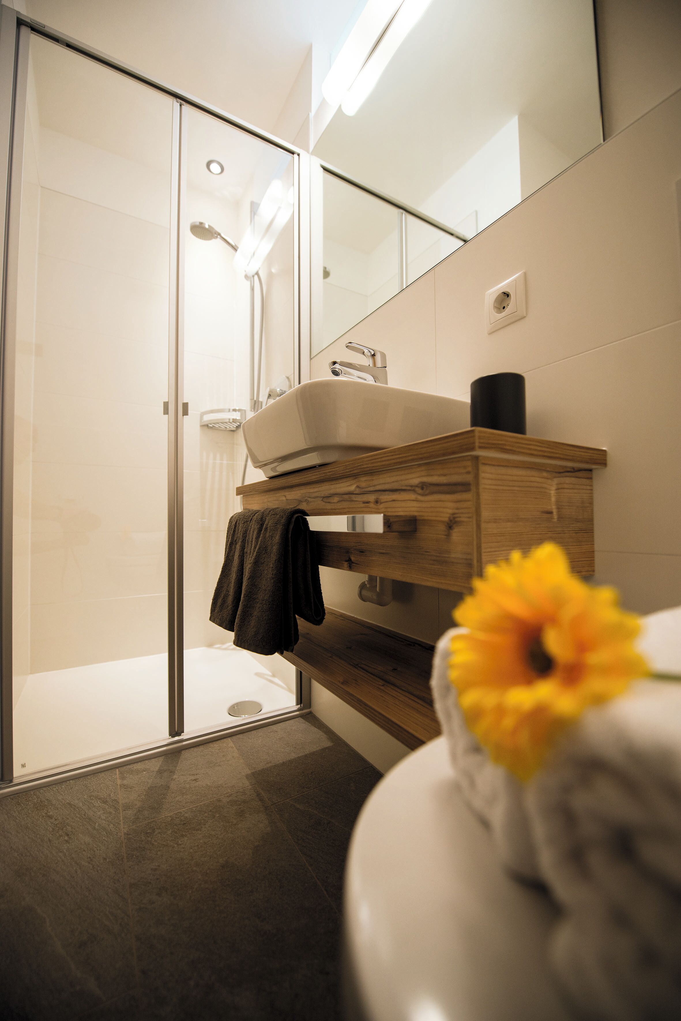 A modern bathroom with a glass shower enclosure, a wooden vanity, and a white sink.