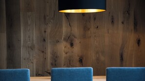 A wooden wall with visible cracks and a hanging light fixture above a table with blue chairs. - Brixen-Plose! Your spacious family apartment directly in St. Andrä (Sankt Andrä)