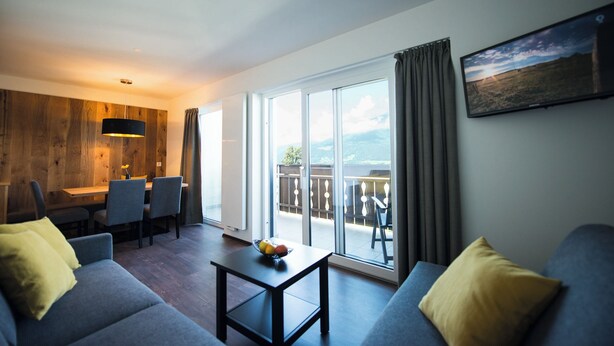 A modern living room with a sofa, a coffee table with fruit, a dining area with chairs, and a balcony with a view. - Brixen-Plose! Your spacious family apartment directly in St. Andrä (Sankt Andrä)