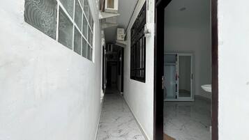 A narrow hallway with a tiled floor, a door leading to a bathroom, and a window with decorative glass.