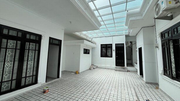 Una habitación amplia con techo alto y tragaluz, con piso de baldosas y ventanas grandes con diseños decorativos en el vidrio.
