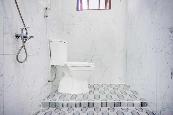 Une salle de bain avec des toilettes, une douche et une petite fenêtre.