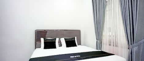 A neatly made bed with a white and black bedspread, a grey headboard, and grey curtains.