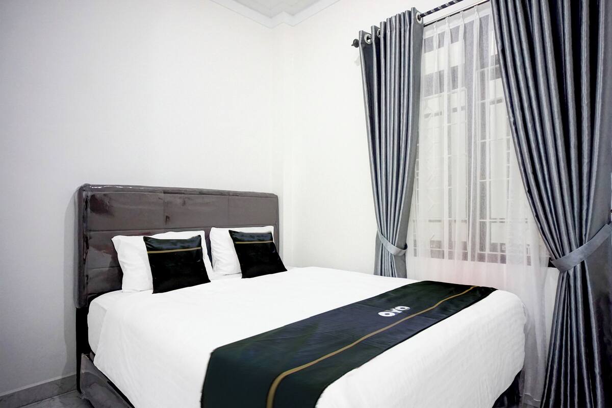 Cama bem arrumada com colcha branca e verde, cabeceira escura e dois travesseiros.
