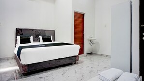 Un dormitorio con una cama, una puerta de madera, un lavabo y una pared blanca.