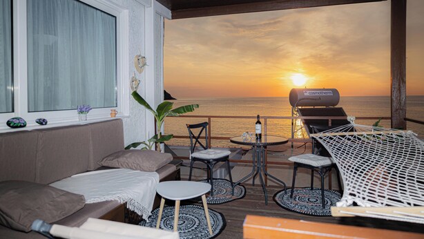 A cozy outdoor seating area with a view of the sunset over the ocean, a grill, and a hammock. - Barbara's Apartment Sea View (Stegna)