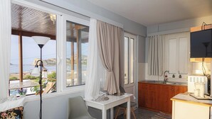 A room with a dining table, chairs, a kitchen area, and a large window with curtains. - Barbara's Apartment Sea View (Stegna)