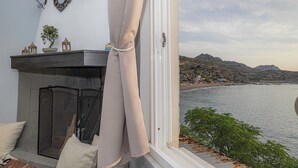A room with a fireplace, a view of the sea, and a balcony with a railing. - Barbara's Apartment Sea View (Stegna)