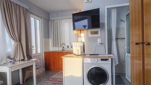 A compact kitchen with a washing machine, a dining table, and a TV mounted above it. - Barbara's Apartment Sea View (Stegna)