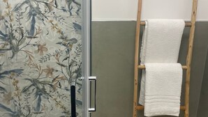 Une salle de bain avec un papier peint à motifs floraux, un porte-serviettes en bois et une porte de douche en verre.