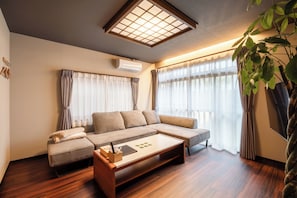 A modern living room with a sectional sofa, a coffee table, and a large window with sheer curtains.