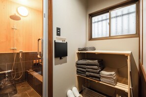Een badkamer met een douchecabine van hout, een handdoekrek en een raam met gezandstraald glas.