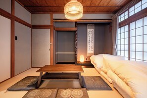 Een traditionele Japanse kamer met tatami vloerbedekking, een lage houten tafel, een bed met witte beddengoed en een shoji schuifdeur.