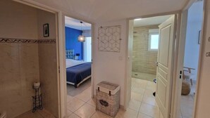 Ein Flur, der in ein Schlafzimmer mit Bett, ein Badezimmer mit Toilette und eine Duschkabine führt.