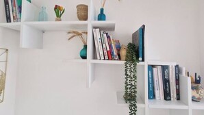 Eine weiße Wand mit drei weißen Regalen, auf denen Bücher und Dekoration stehen.