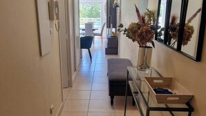 Ein Flur mit einer Bank, einem Tisch mit einer Vase getrockneter Blumen und Blick auf einen Außenbereich mit Tisch und Stühlen.