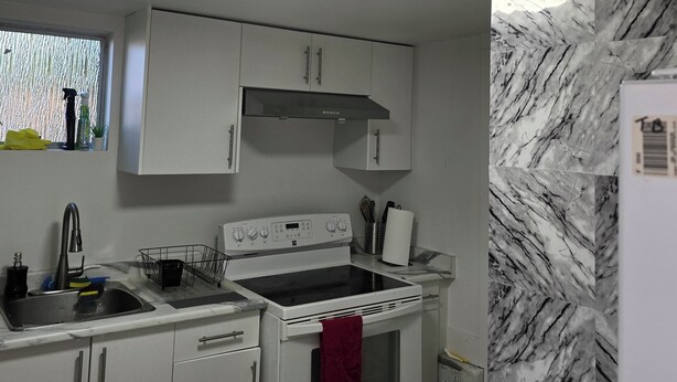 A compact kitchen with white cabinets, a stainless steel sink, a stove, and a marble backsplash. - Private bedroom (2) in shared suit (Delta)