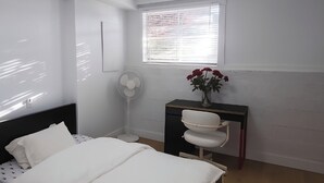 A bedroom with a bed, a desk, a chair, a fan, and a window with blinds. - Private bedroom (2) in shared suit (Delta)