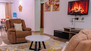 Un salon avec un canapé, une table basse et un téléviseur diffusant une image de cheminée.