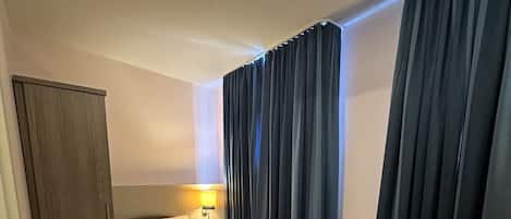 A hotel room with a bed, a desk, a wardrobe, and a window with curtains.
