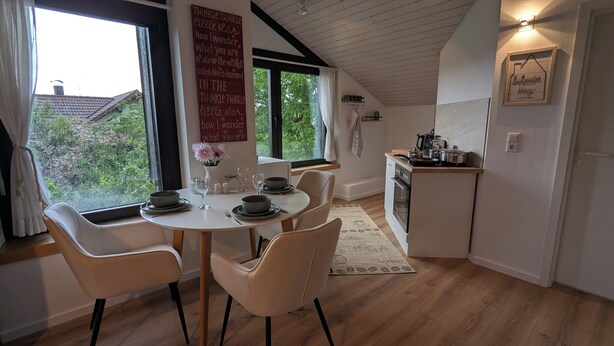 A cozy dining area with a round table, white chairs, and a view of greenery outside. - 2 room apartment touring view at the Kaiserberge motorcycle / bicycle garage (Waldstetten)