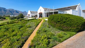A modern building with a paved pathway leading to the entrance, surrounded by lush greenery and mountains in the background.